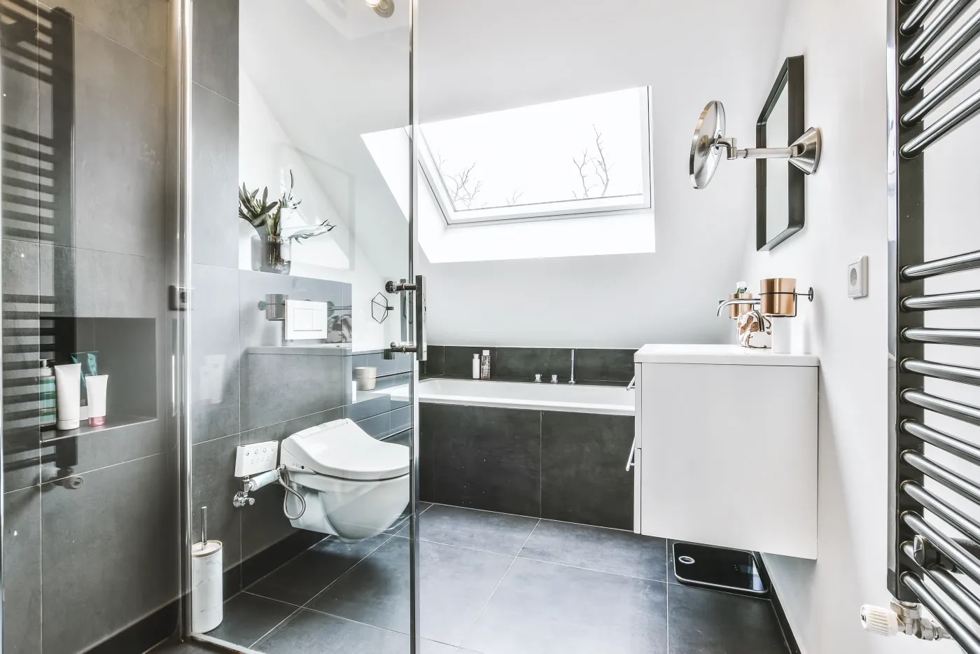 Modern black-and-white bathroom with a bathtub under a sloped ceiling, a wall-mounted toilet and vanity cabinet, and a heated towel rail on the wall