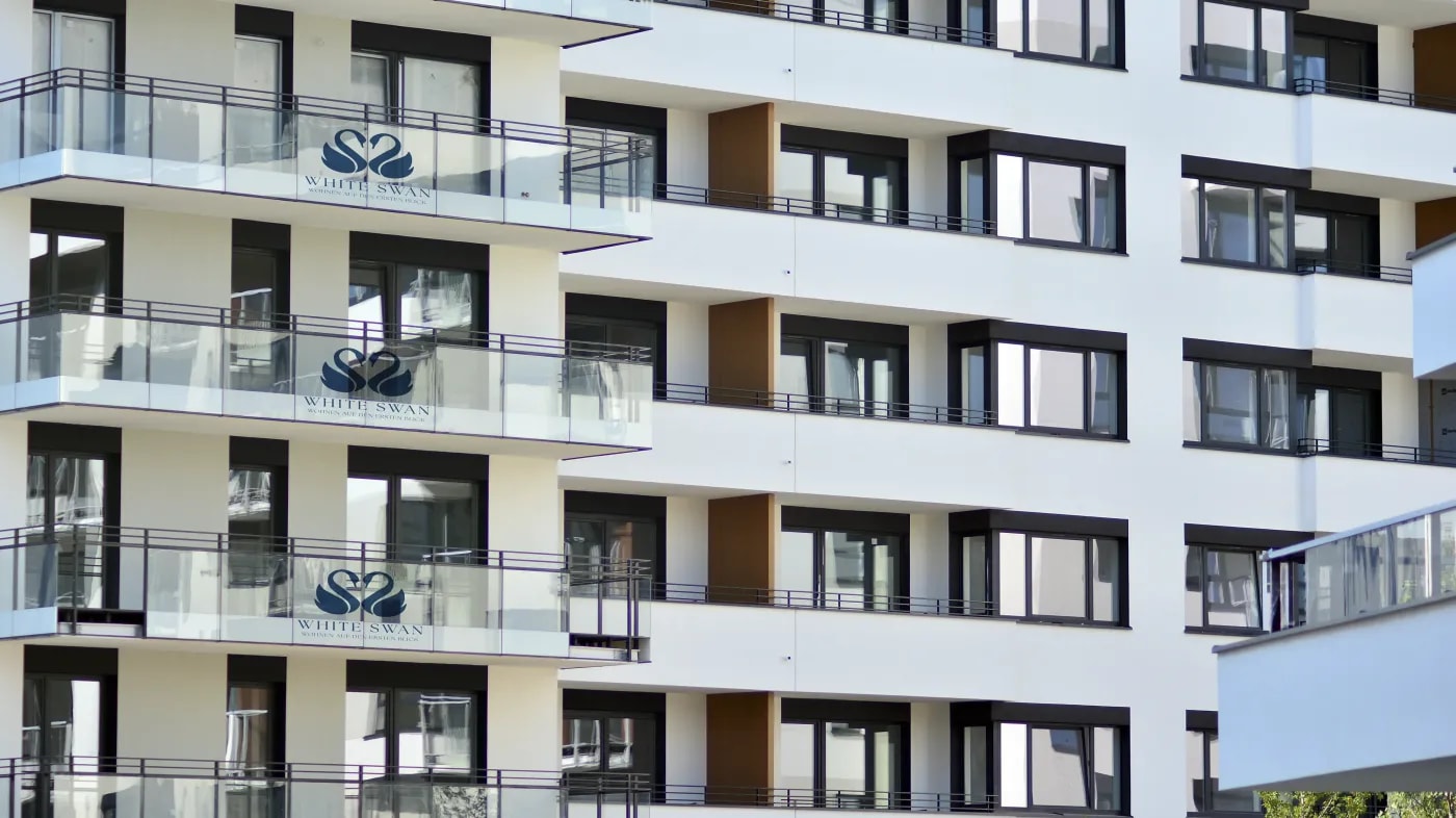 Detail shot of the facade of the 'White Swan' property with balconies, showing the property's logo on the glass panel railings