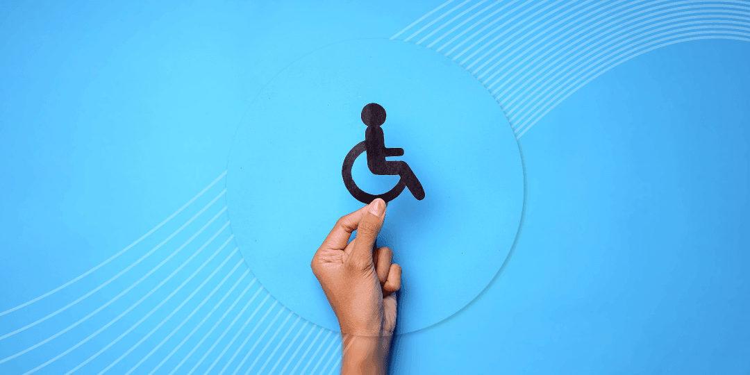 Hand holding a dark cut-out of the international wheelchair symbol against a bright blue background with graphic arc patterns.