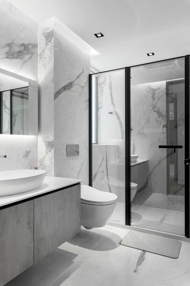 Modern bathroom in marble and light gray wood with a walk-in shower with glass surround, a toilet, and a floating vanity cabinet