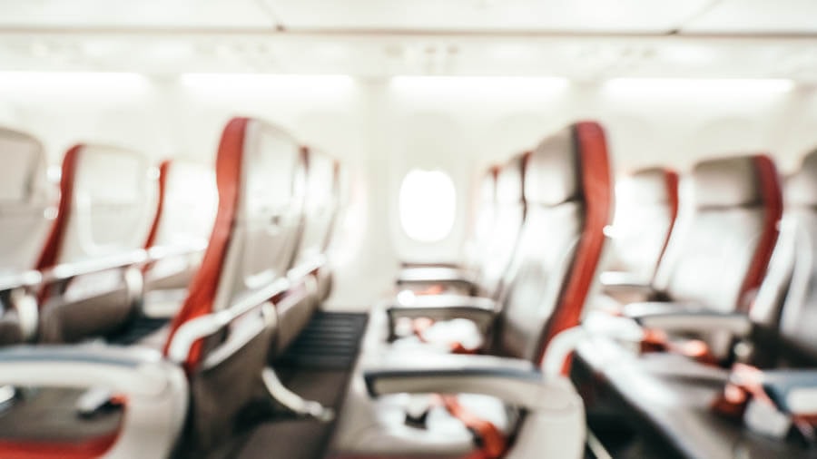 Blurred interior shot of an aircraft showing typical rows of three seats.
