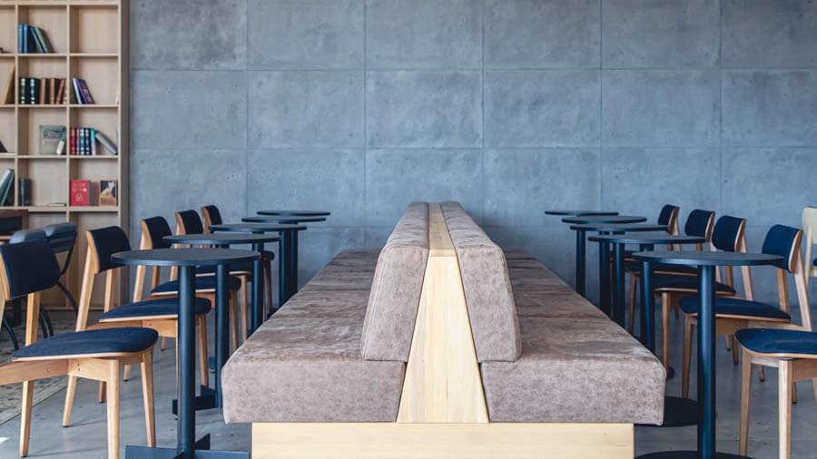 Side view of beige bench seats arranged back to back, with black canteen tables in front and a single chair at each table.