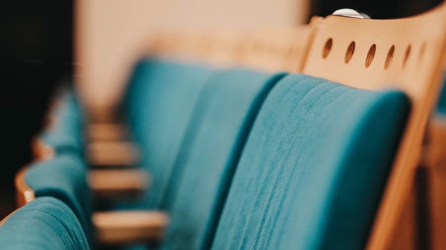 Close-up of a row of teal upholstered folding seats in a cinema or theatre.