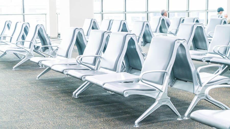Angled view of rows of metal seats in a typical airport terminal with a wide window front in the background.