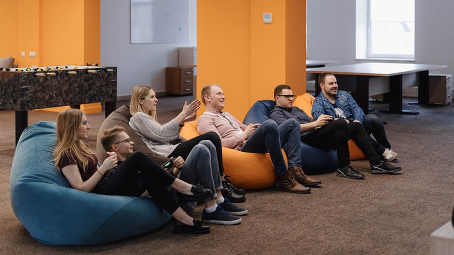 Several people seated on orange and dark blue beanbags listening to a talk in a youth room with a table football table and tables in the background.