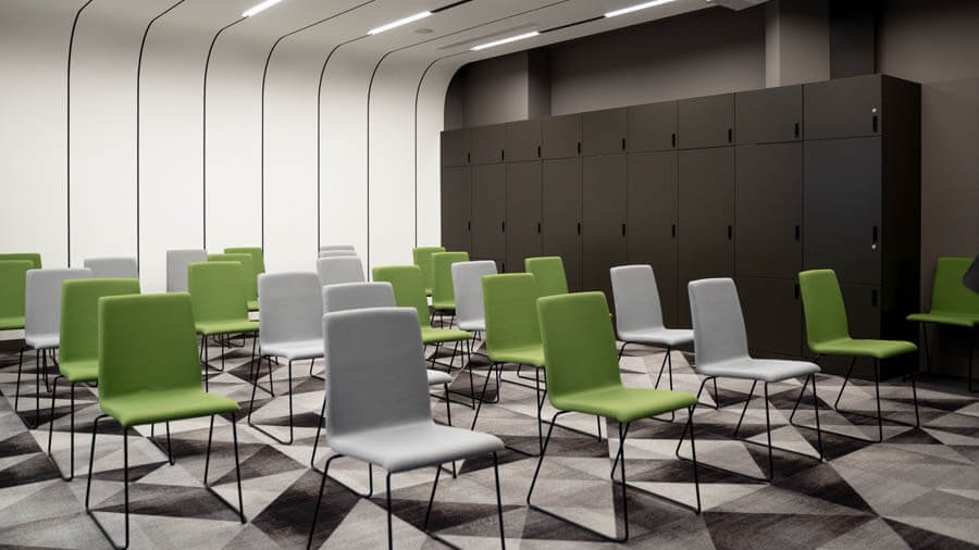 View into a modern lecture room with white and green chairs and a black cabinet to one side.