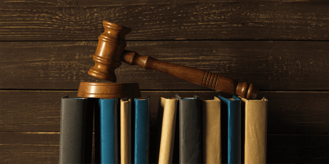 A judge's gavel lies across a row of law books against a dark wooden background.