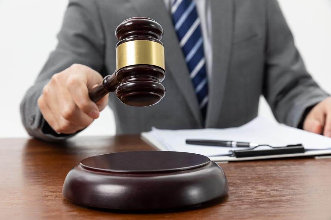 Close-up of an auctioneer with a raised gavel at a wooden podium, in front of which a clipboard with documents is lying