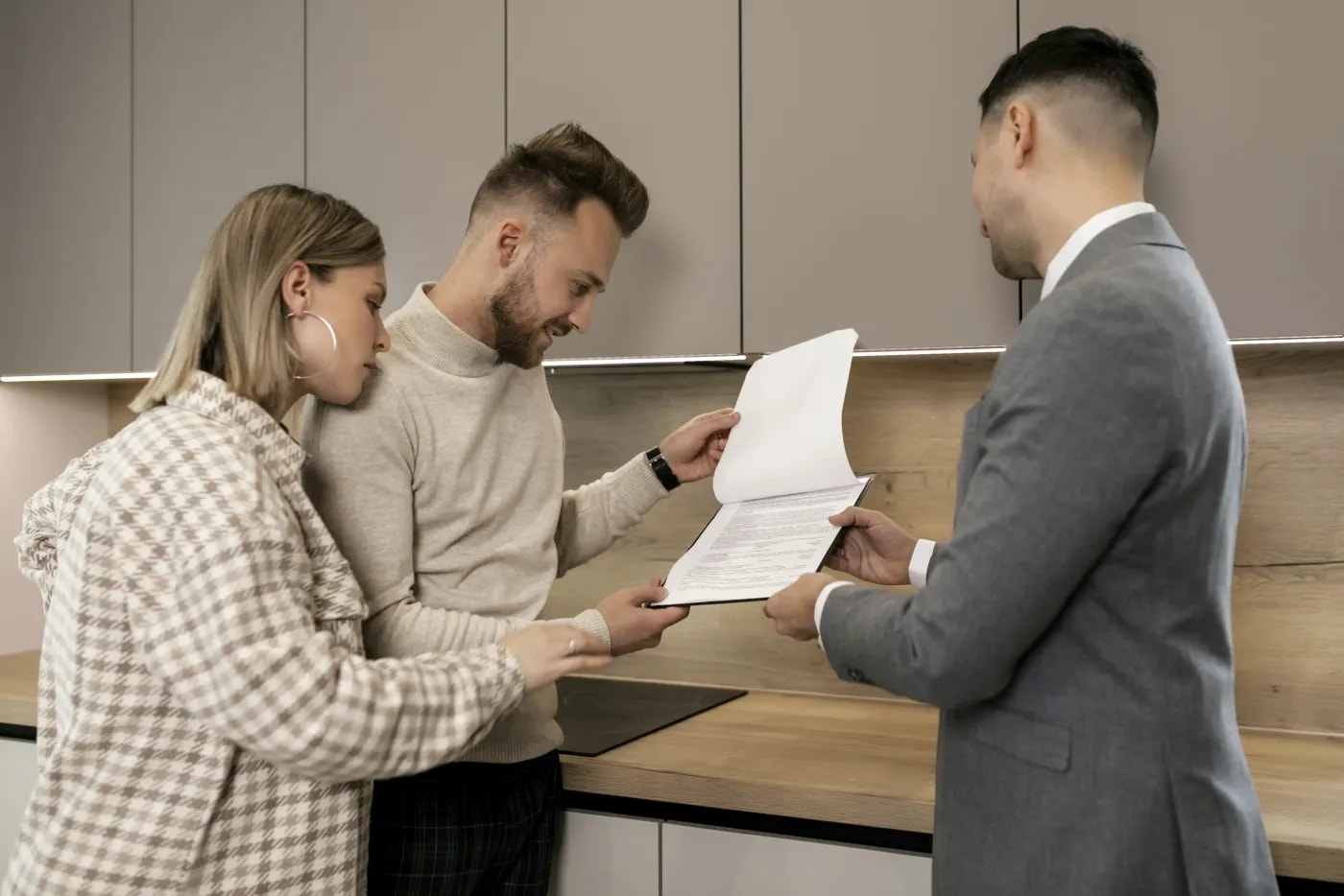 A real estate agent stands with an interested couple in the kitchen, showing them a list of information about the property