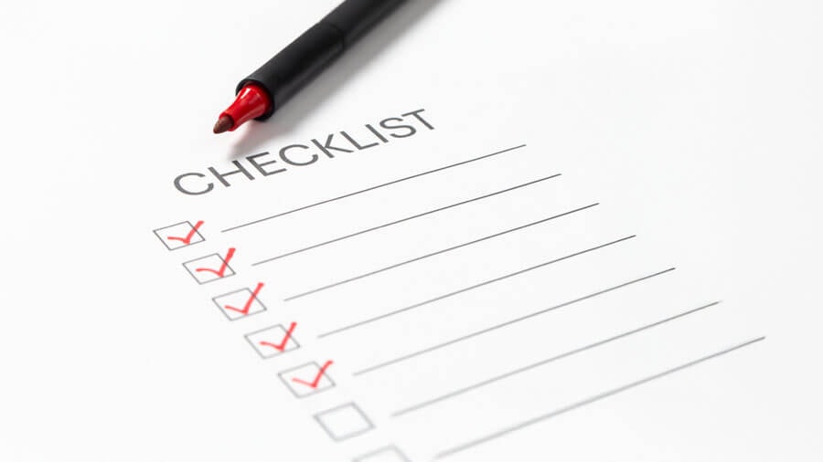 A printed checklist with an uncapped red pen resting on it, with several items ticked off in red.