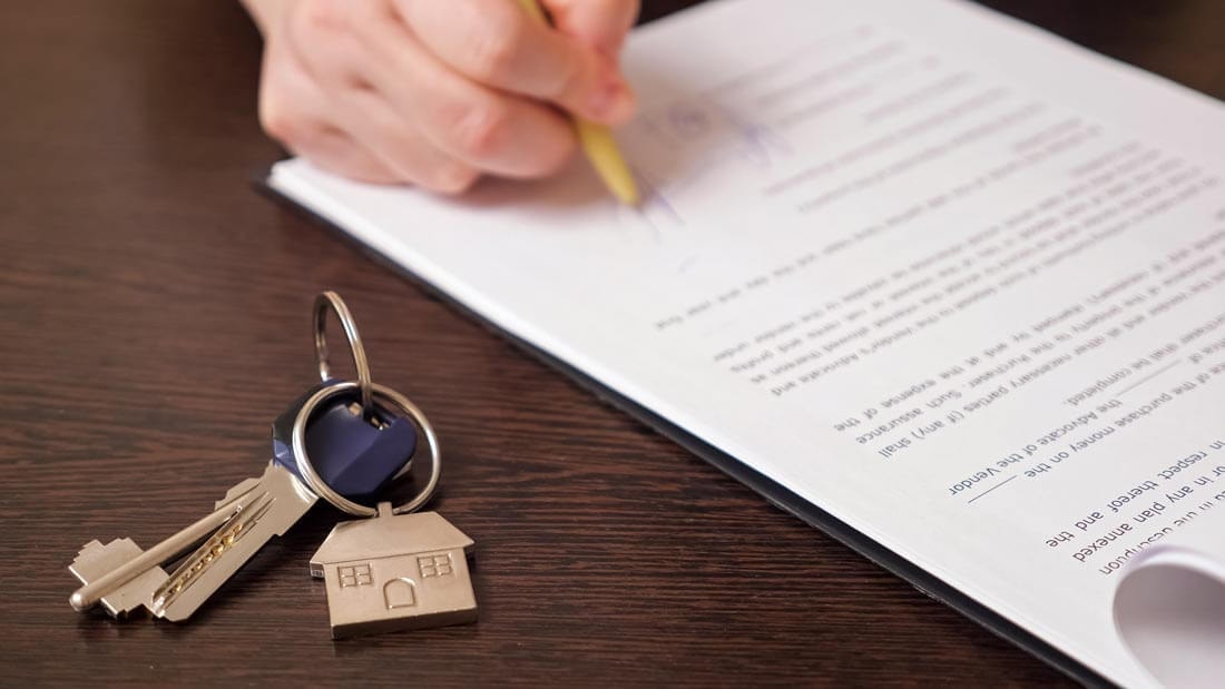 Close-up of a contract on a dark wooden desk being signed, with the apartment keys already lying ready next to it