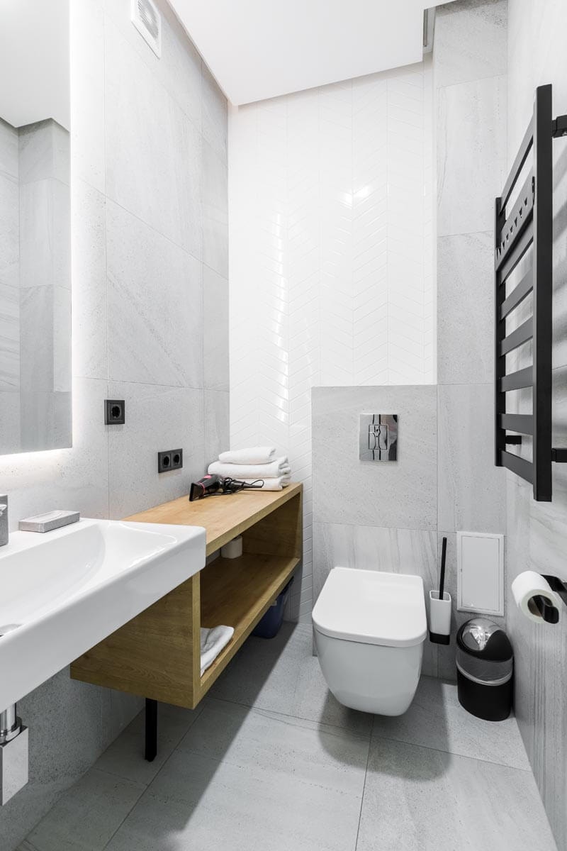 Small, modern guest toilet in gray-and-white with wood accents, featuring a washbasin and large mirror on the left and a heated towel rail on the right wall