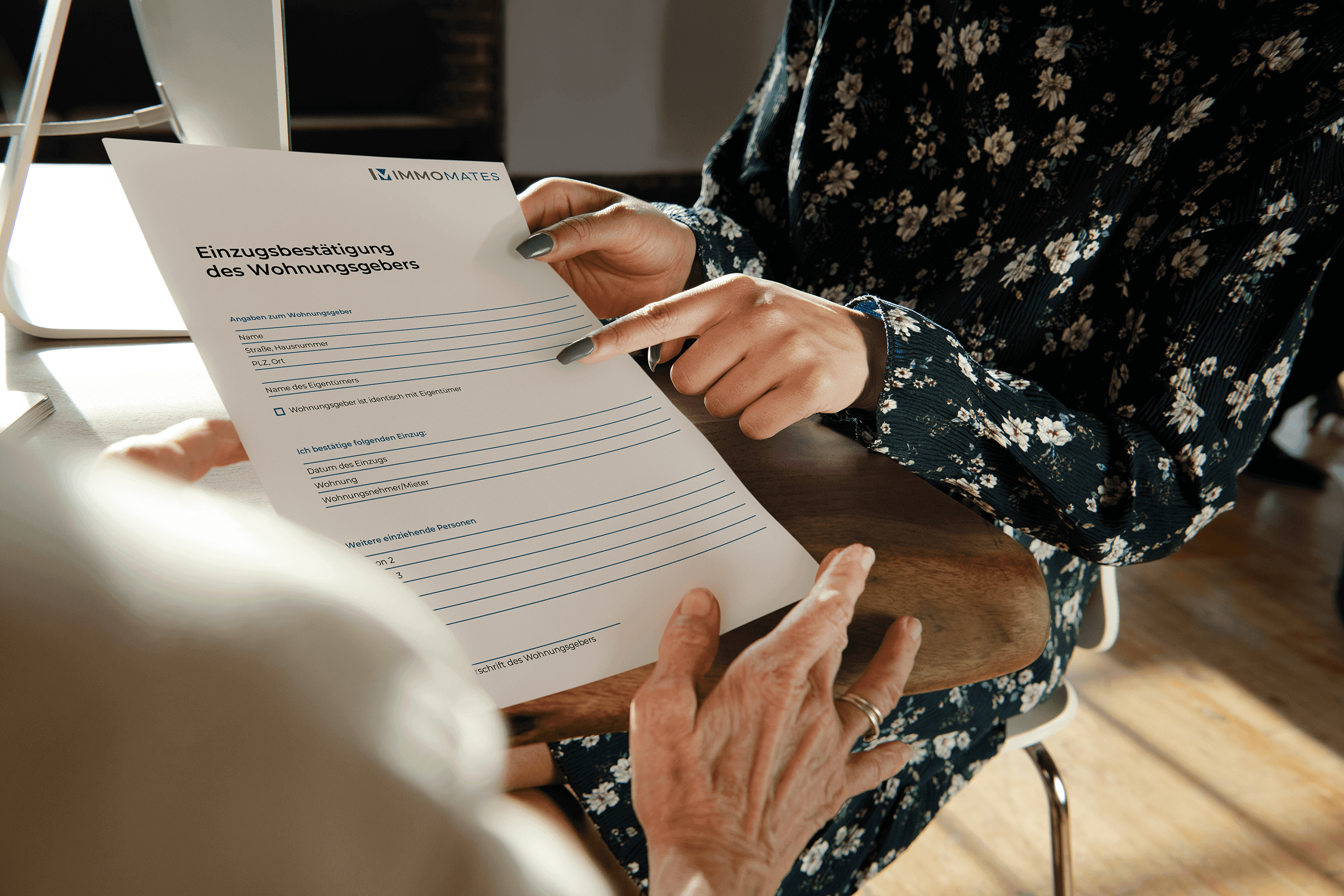 A female estate agent in a floral dress shows a client the landlord's confirmation of residence form and points to the text with her index finger.