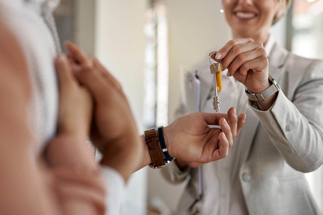 Close-up of a key handover, with a real estate agent smiling as she hands a key to a couple