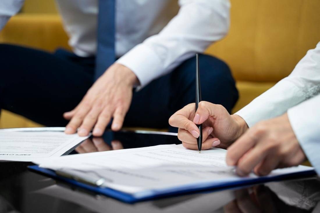 Close-up of two people at a table, one of whom is signing a contract