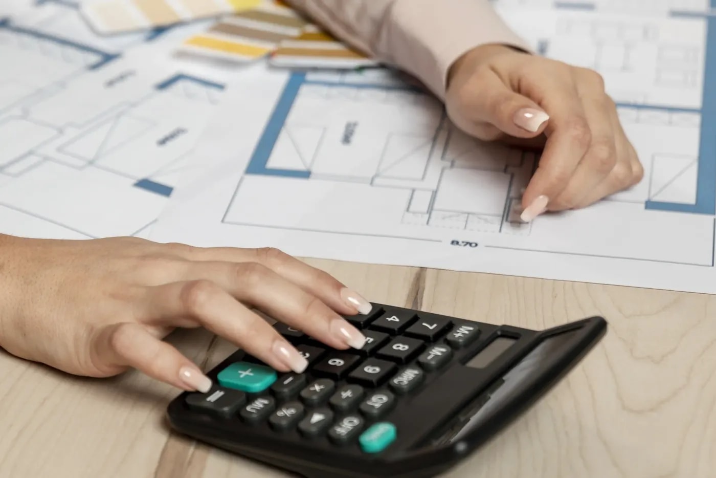 Close-up of a desk with floor plans lying on it and a hand entering something into a calculator