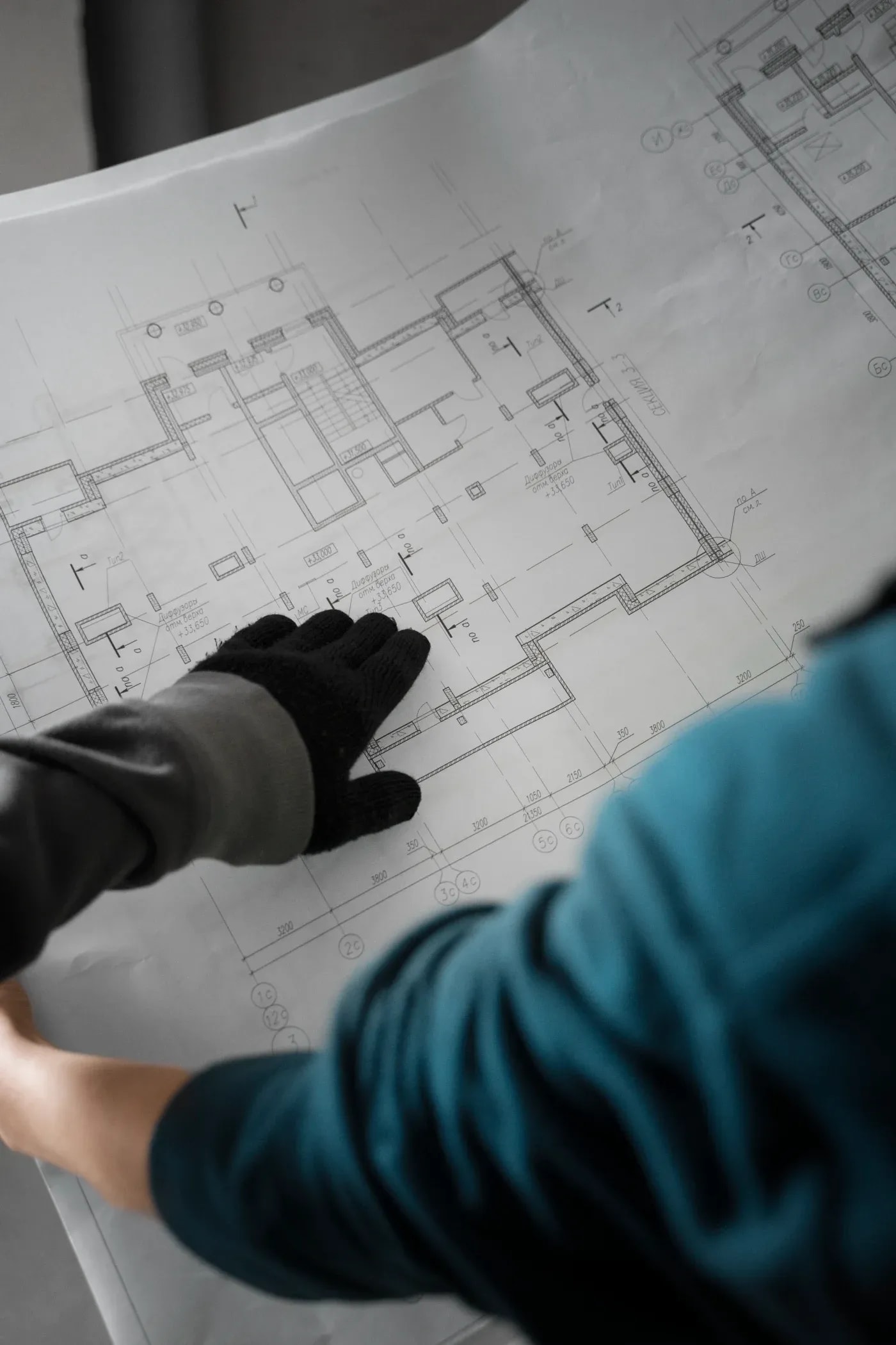 Over-the-shoulder view of a person holding a large dimensioned floor plan and pointing to a detail.