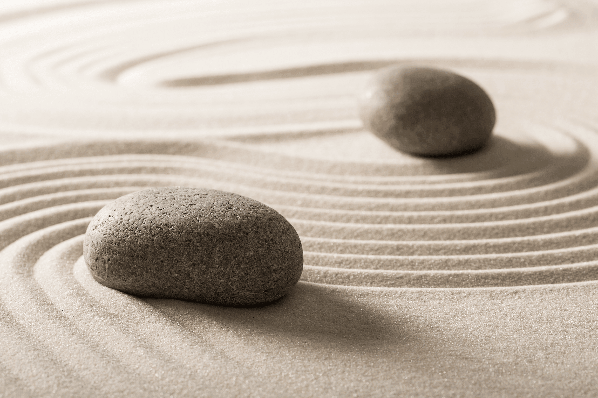 Two smooth stones in a Zen garden with concentric groove patterns raked in sand, symbolising harmony and balance.
