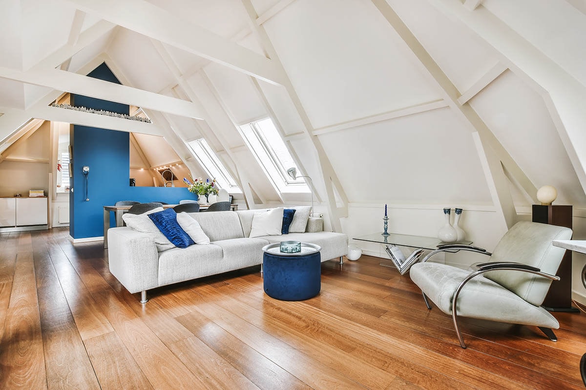 Converted attic with wooden flooring, a living room in the foreground and an open kitchen visible in the background.
