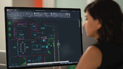 View from behind of a woman editing a floor plan displayed on a monitor.