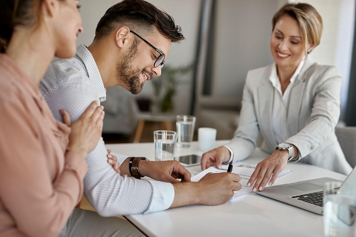 Smiling couple signing a loan agreement in the presence of a bank advisor