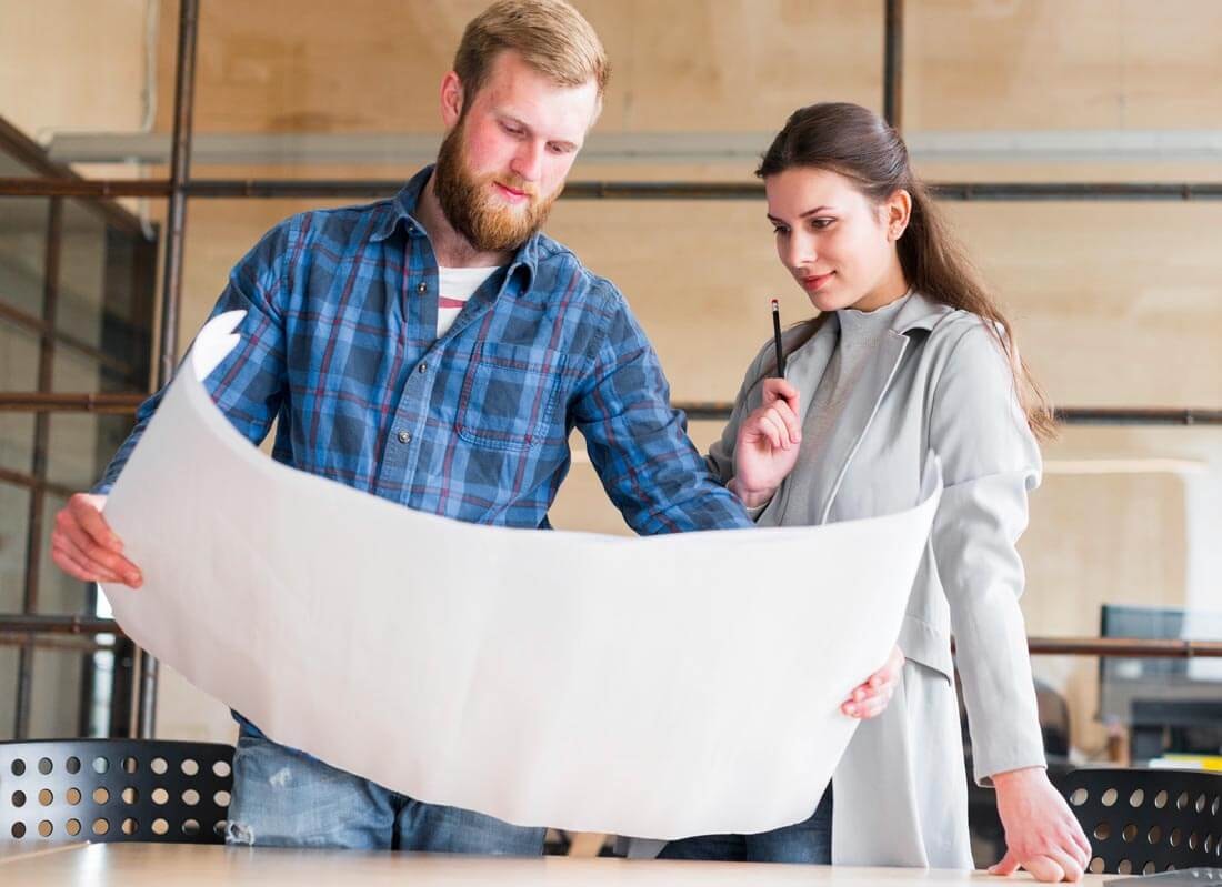 Man and woman examining a large architectural plan together at a table in an office