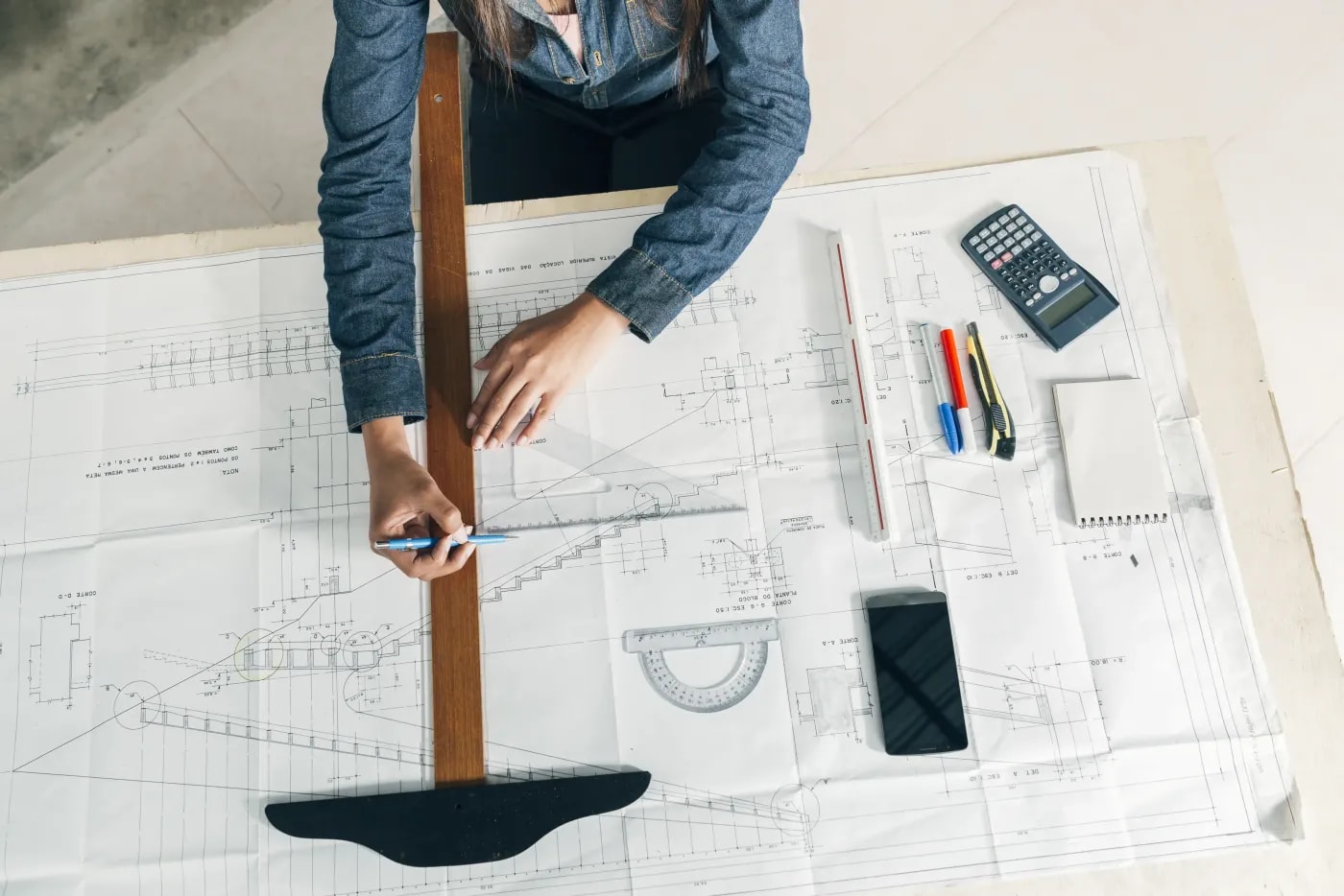 A woman uses two rulers to draw something on a staircase in a construction drawing