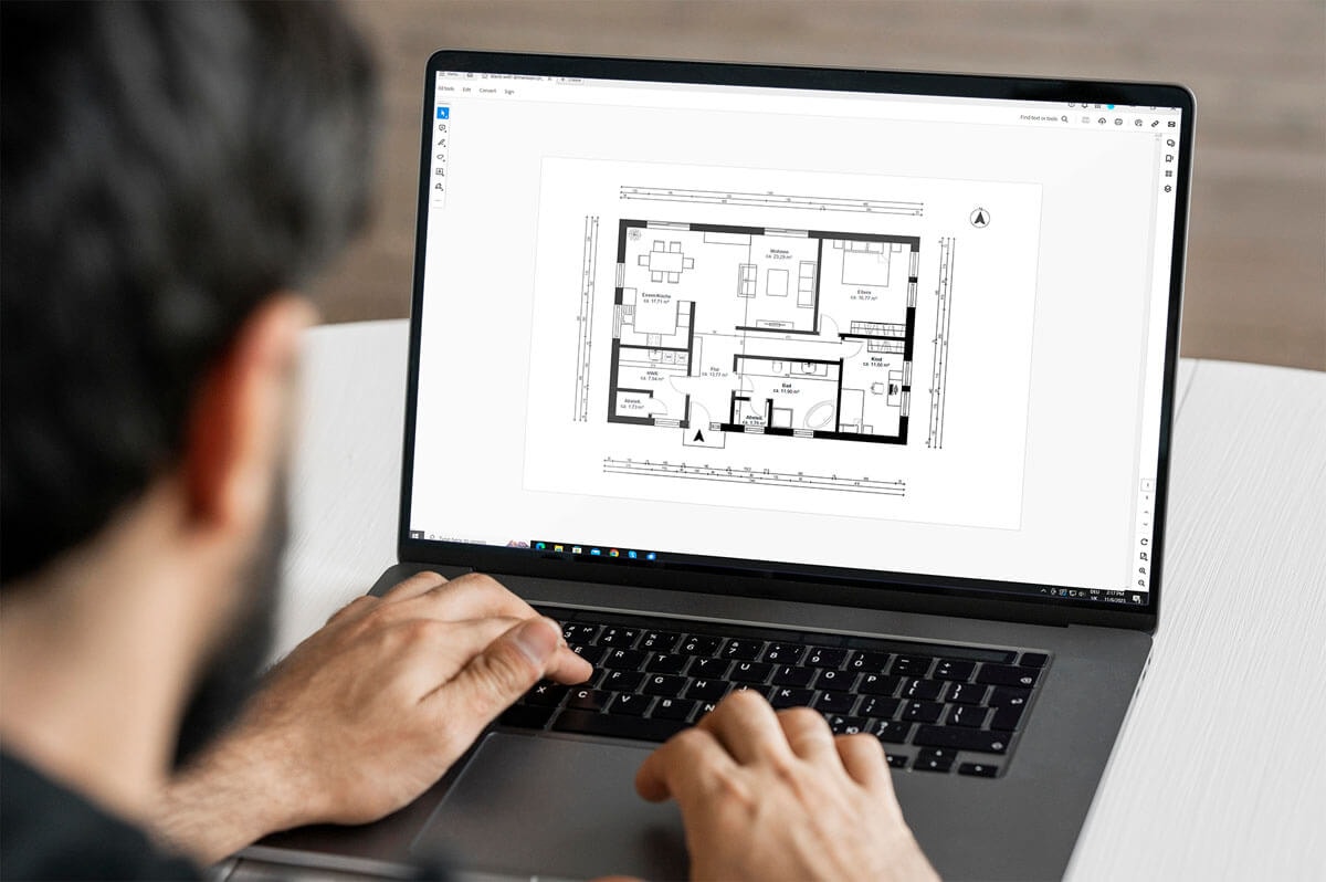 Rear view: a man sits at a laptop with his hand on the keyboard, studying the dimensioned floor plan of a 3.5-room apartment.