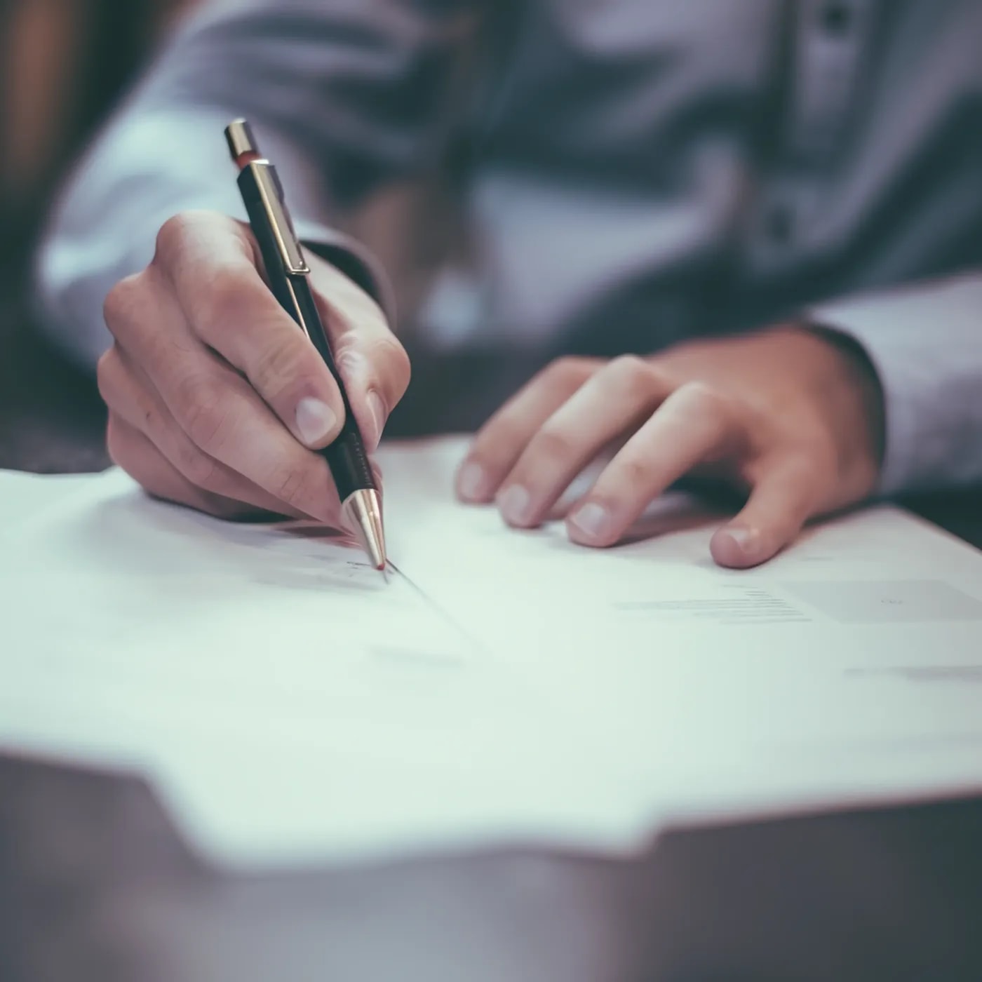 Close-up of someone signing a document with a ballpoint pen.