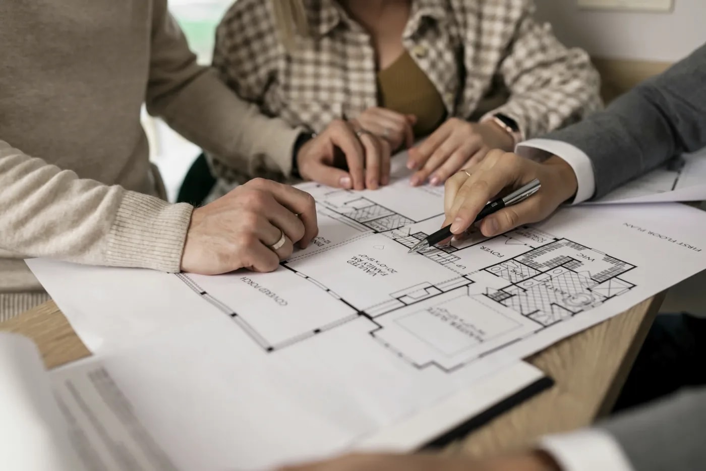 An estate agent pointing out a detail on a floor plan to their clients using a pen.