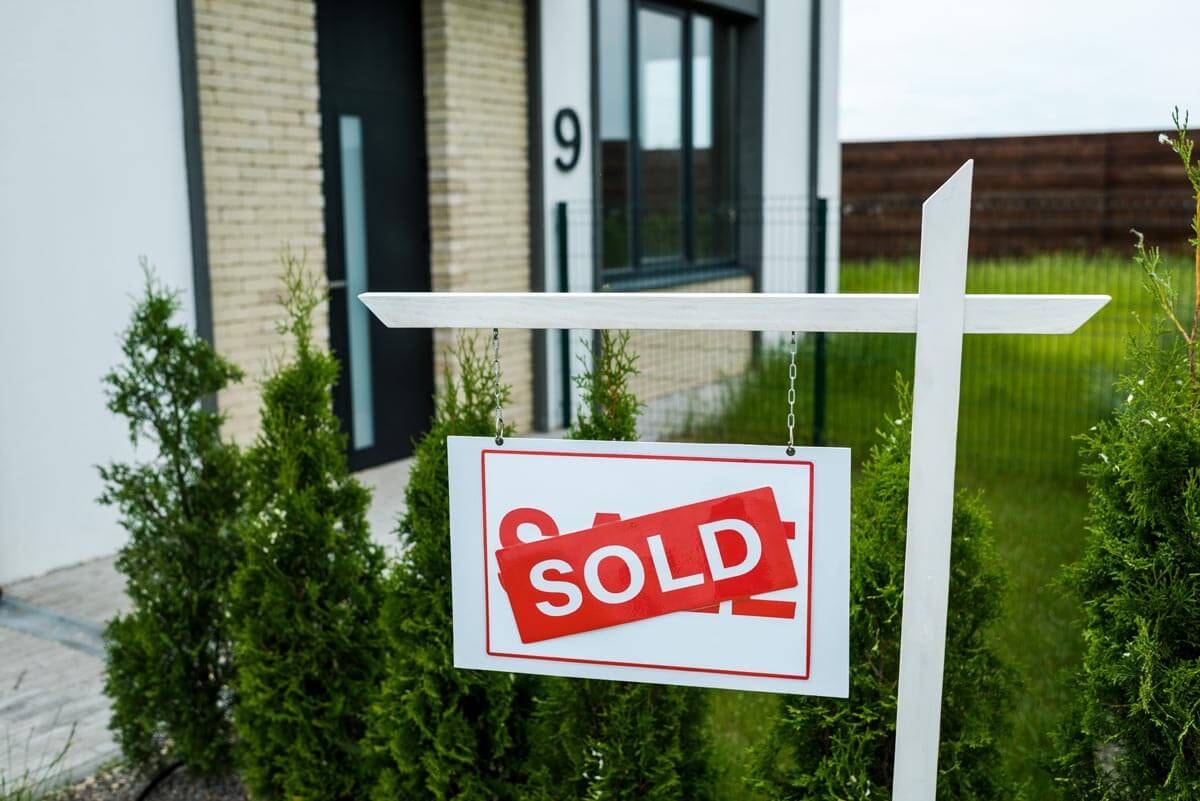 Close-up of a white 'Sold' sign with red lettering in front of a house numbered 9