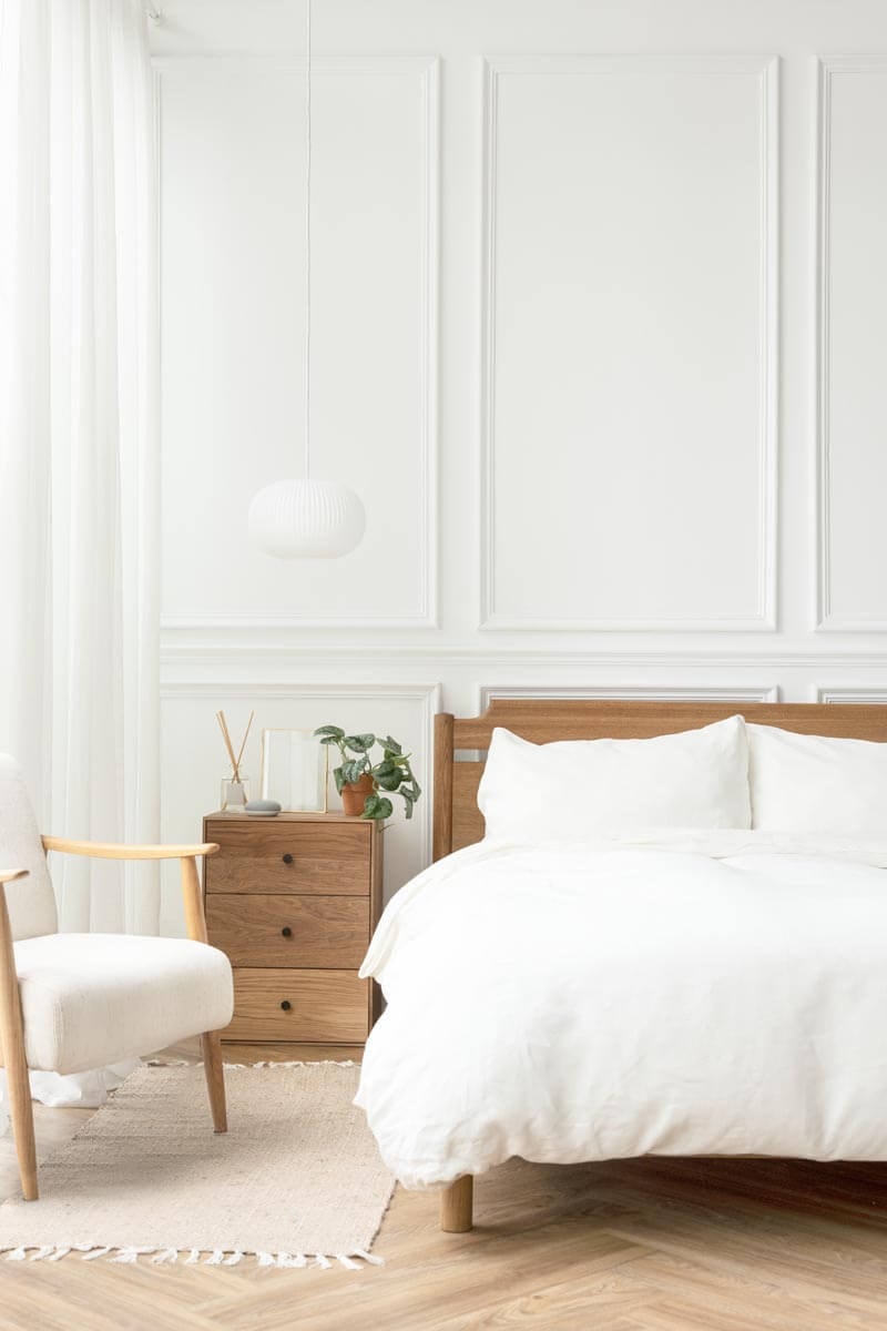 Bright bedroom in Scandinavian style with white wall panelling and oak furniture.