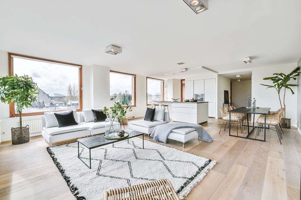 Corner view into a spacious living room with an open kitchen, large windows and a low ceiling.