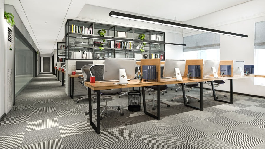 Shot of an open-plan office from the corner of the room with several rows of desks, each with four workstations per row, and floor-to-ceiling shelving units as room dividers after every eight workstations.