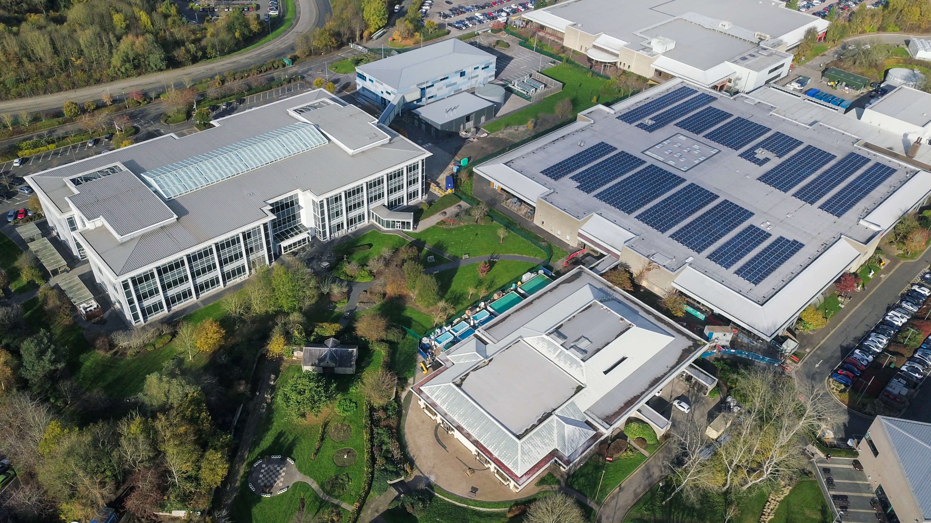 Aerial view of a larger industrial building complex, one of which has solar panels on the roof.