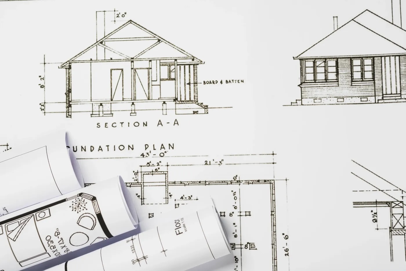 Close-up of documents showing the floor plan and facade elevation of a bungalow alongside other rolled-up plans.