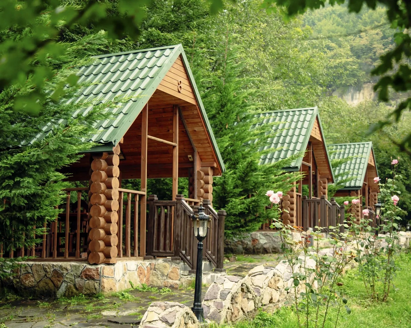 Front view of three identical bungalows with green pitched roofs nestled among fir trees with a rocky hillside in the background.