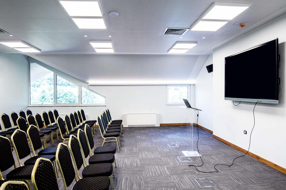 Side view of rows of black chairs lined up in front of a large wall-mounted monitor.