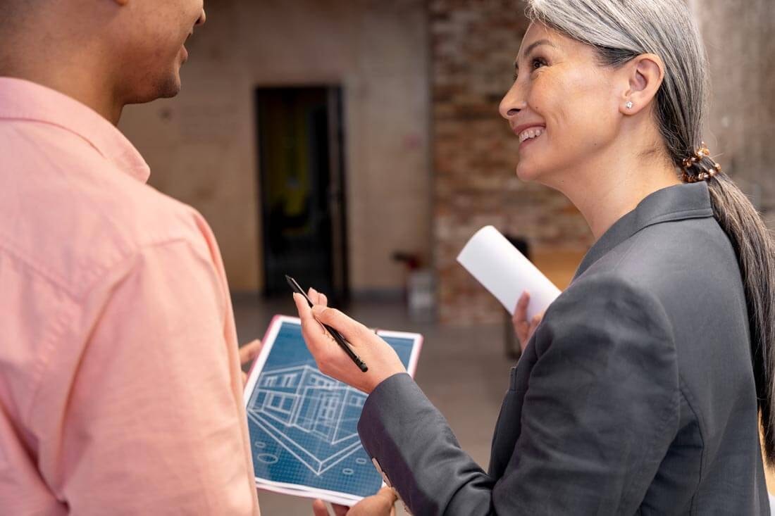 Female architect discussing a digital building plan on a tablet with a client in front of a shell construction