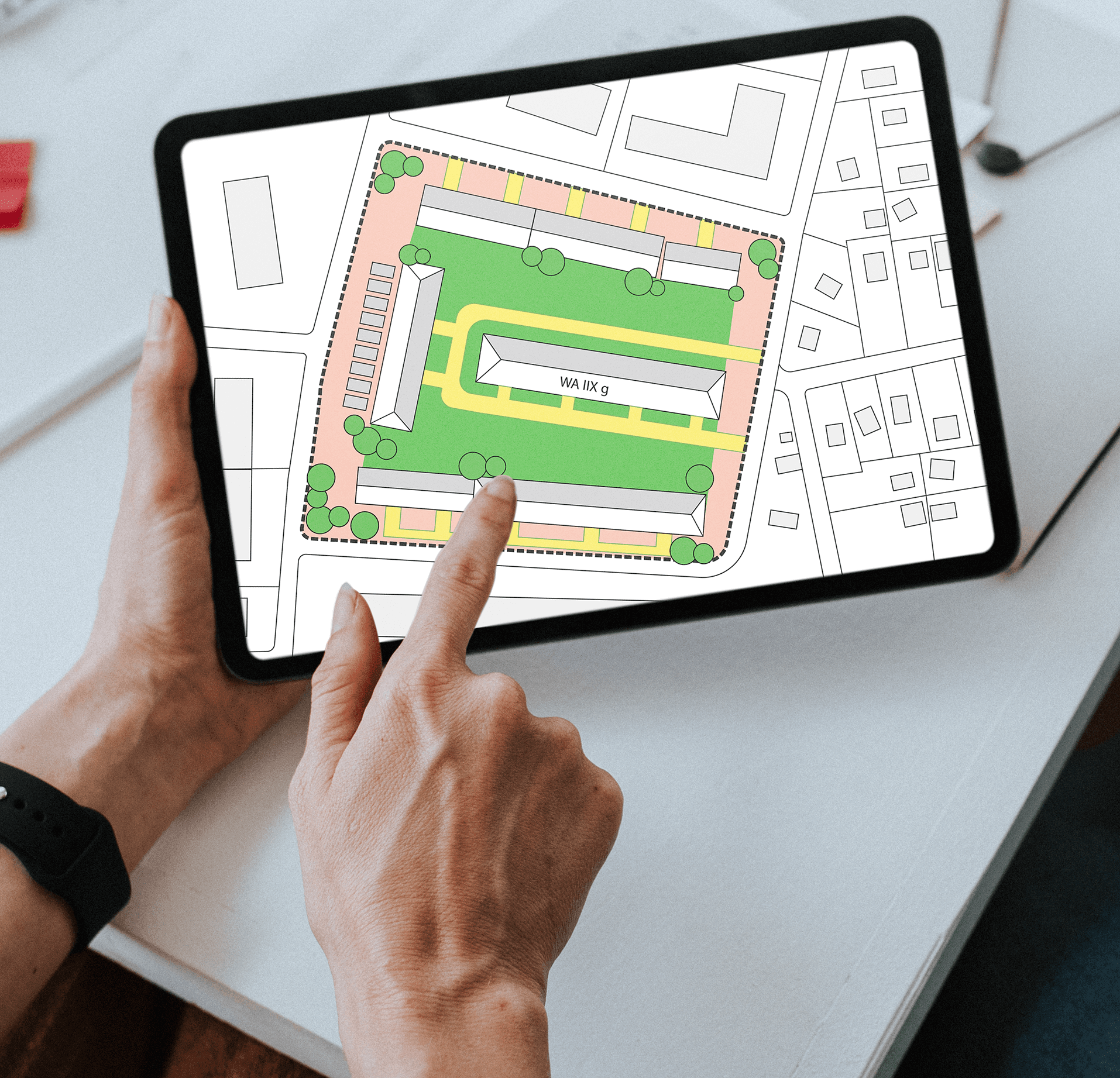 Close-up of a tablet showing a colored zoning plan for an office building complex situated next to a green space, with parking areas marked around it