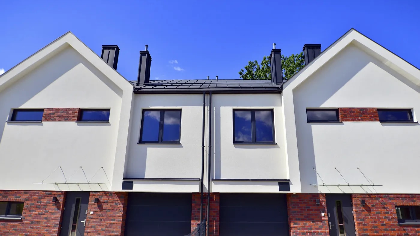 Modern, symmetrical semi-detached house with brick and render facade, garages next to the entrances, pitched roof and a single window at the front.