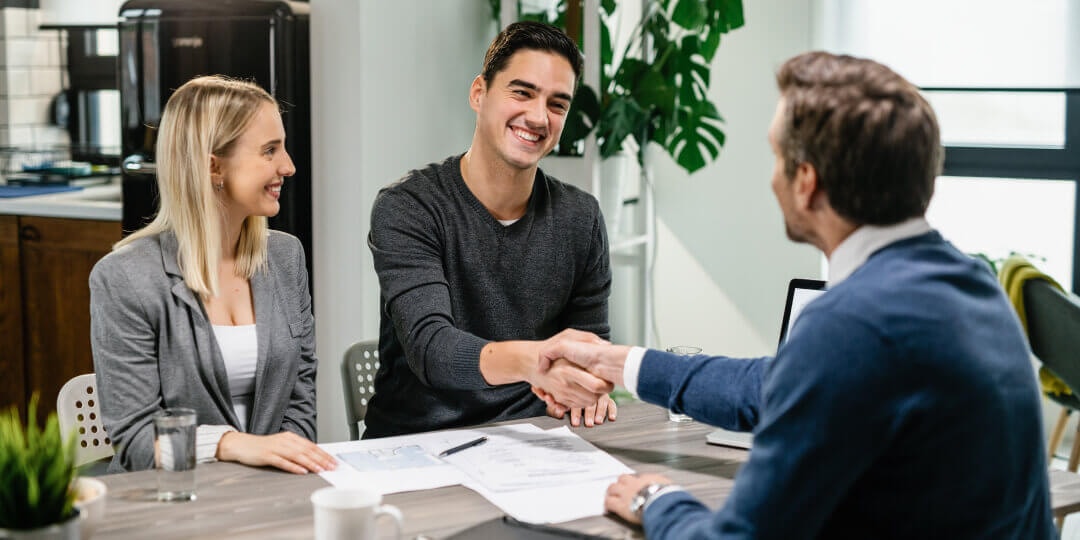 Young couple at a successful contract signing: smiling and shaking hands with a consultant at the table.