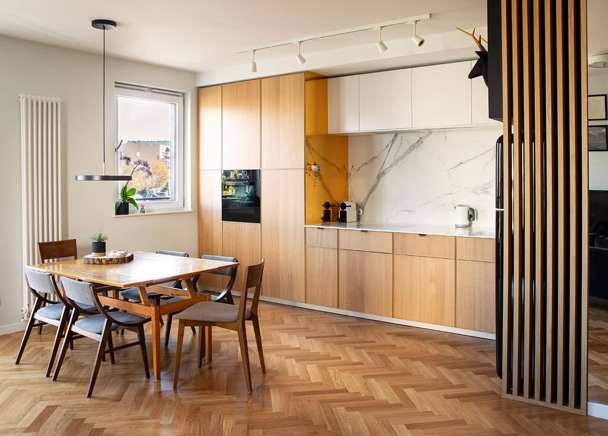 Side view of an open kitchen with an oak-look kitchen unit and a light-colored countertop, with a dining table positioned in front, centered in the room