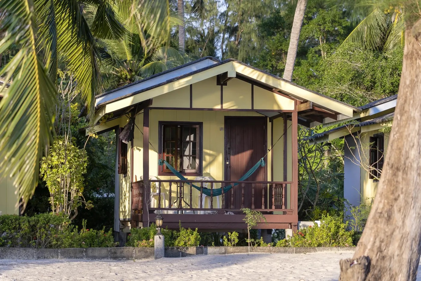 Front view of a tiki-style bungalow surrounded by palm trees and bamboo on a beach.