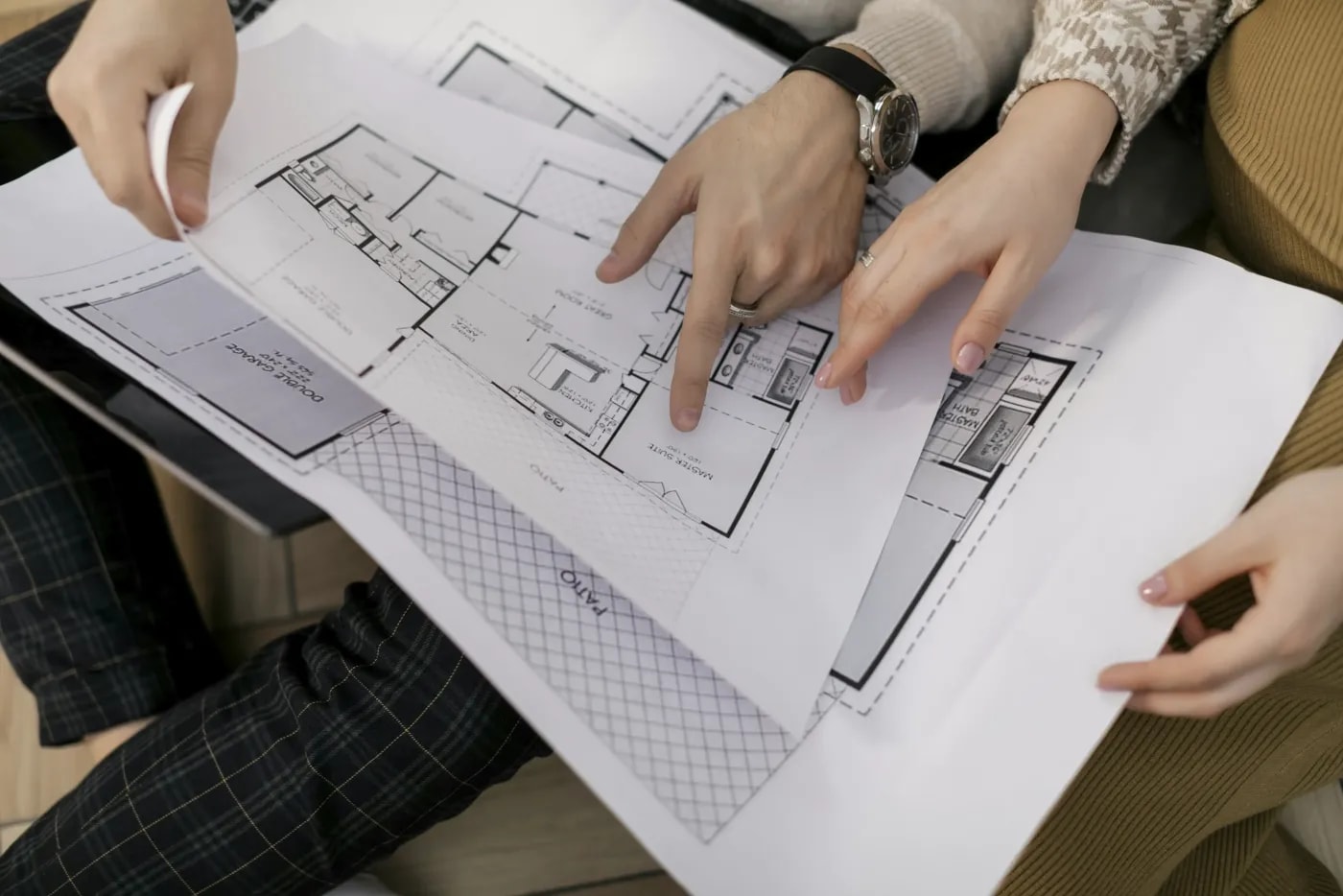 Two people holding overlapping floor plans of an apartment in two sizes on their laps, pointing at one of the living spaces