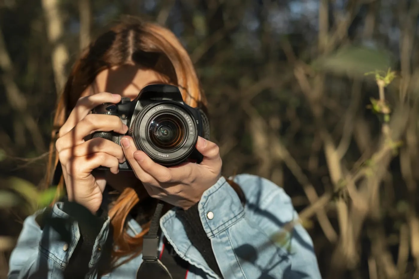 A photographer stands among bushes taking a photo of something behind the viewer