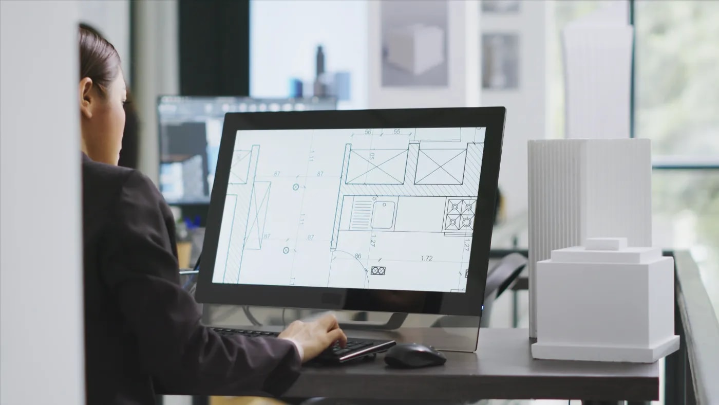 Ansicht von hinten auf eine Frau, die sich auf einem Monitor den Detailausschnitt der Küche eines Grundrisses anschaut.