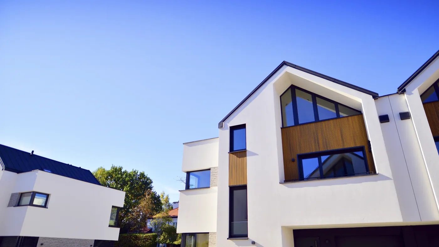 Frontansicht eines modernen Neubaus einer Doppelhaushälfte mit einer Fassade aus größtenteils hellem Putz und einzelnen Zierelementen aus Holz und Naturstein.