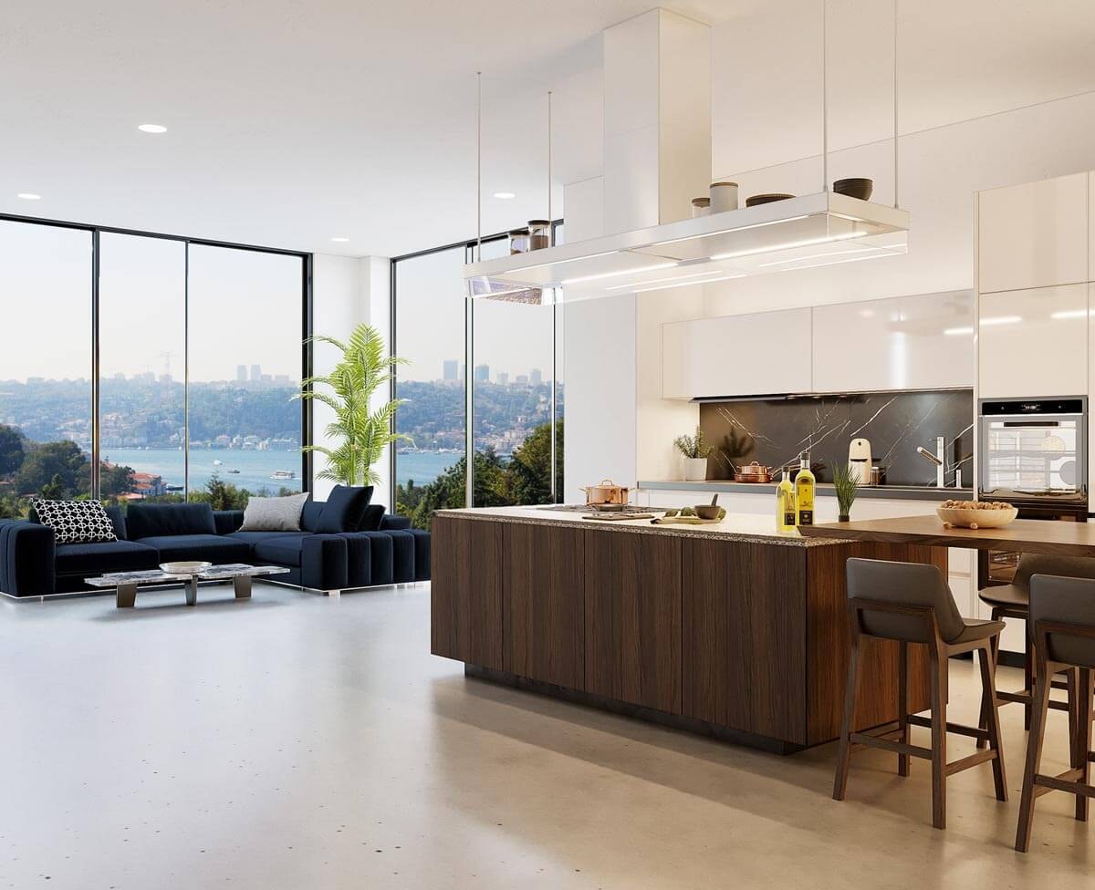 Open, generous kitchen-living area on an upper floor with a freestanding central island housing the hob and dining table, very high ceilings and large panoramic windows beside the seating area through which a bay panorama is visible.