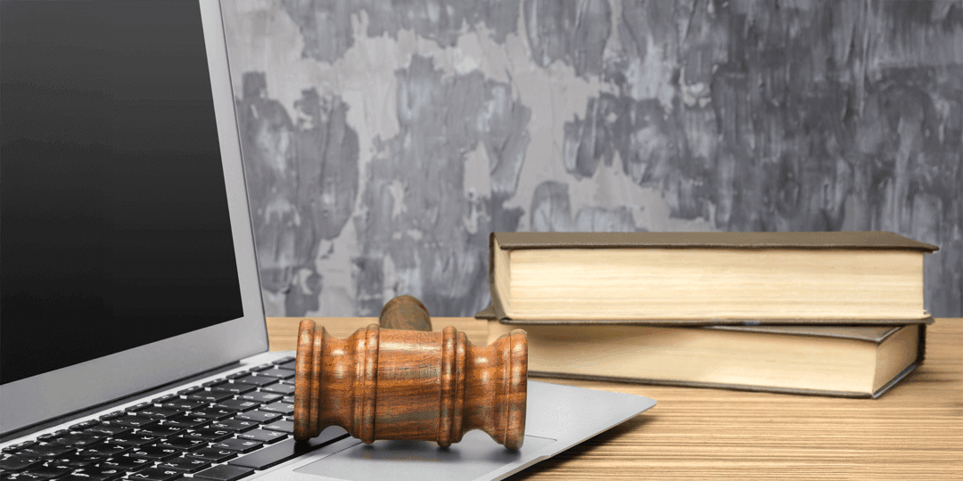 Close-up of a laptop on a table, next to which a wooden gavel and two stacked books are lying.